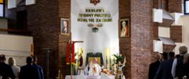 Wnętrze kościoła podczas mszy świętej w intencji strażaków. Przy ołtarzu widoczne są elementy symboliczne związane z Państwową Strażą Pożarną.