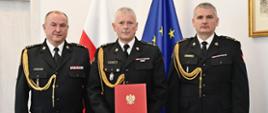 Pomorski Komendant Wojewódzki Państwowej Straży Pożarnej st. bryg. Jacek Niewęgłowski, Zastępca Komendanta Powiatowego Państwowej Straży Pożarnej w Człuchowie bryg. Dariusz Dwulit i Komendant Powiatowy Państwowej Straży Pożarnej w Człuchowie st. bryg. Radosław Batruch stoją na tle flagi państwowej i flagi unii europejskiej.