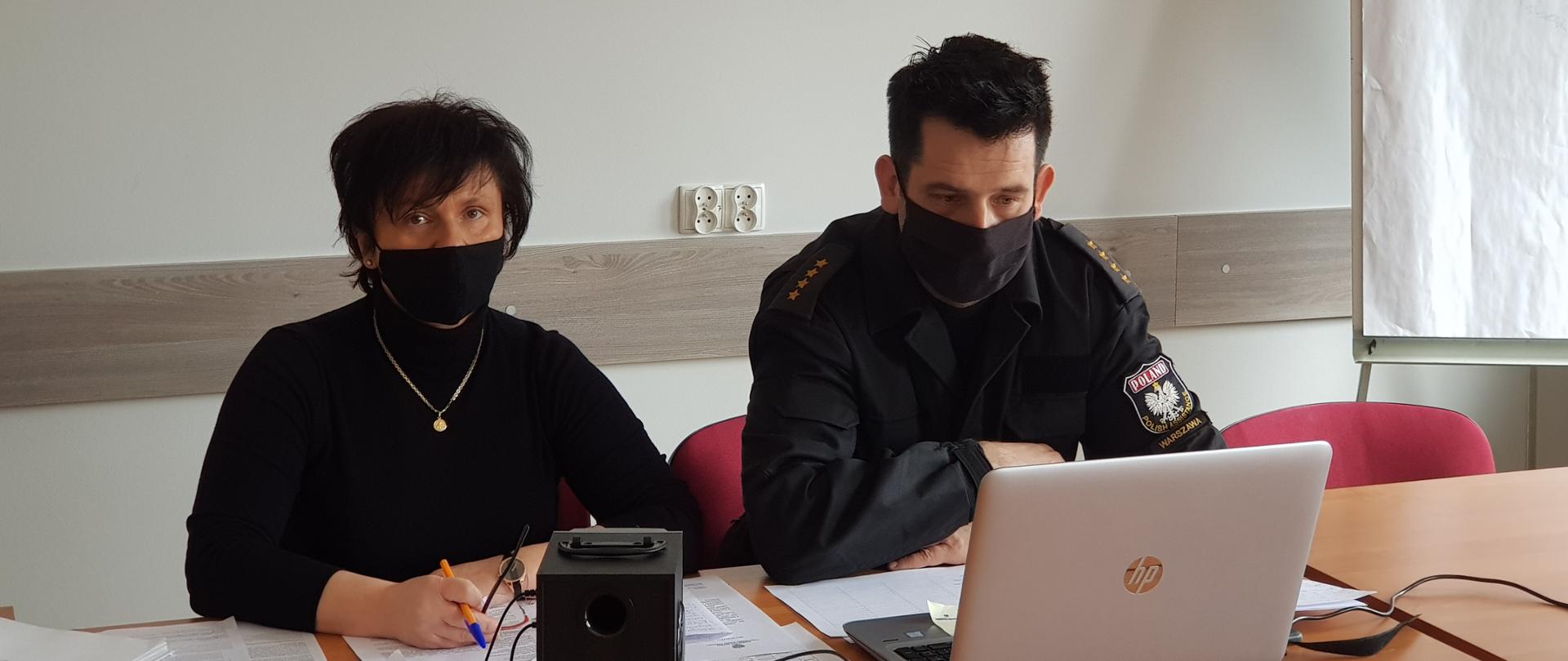 Zdjęcie przedstawia dwie osoby kobietę i mężczyznę , siedzących przed komputerem w pomieszczeniu zamkniętym należącym do Wydziału Ośrodka Szkolenia w Warszawie, podczas wideokonferencji miejskich/powiatowych koordynatorów ratownictwa medycznego PSP woj. mazowieckiego. Spotkanie dotyczy spraw bieżących