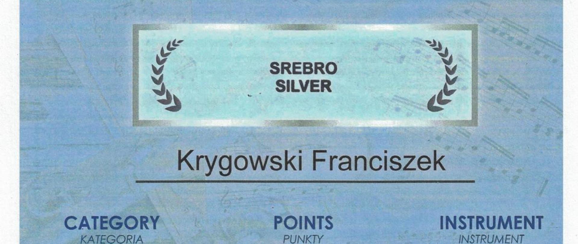 Dyplom na niebieskim tle, na górze napis:
DYPLOM, Finalis V Międzynarodowy Konkurs Instrumentów Dętych 15-18 listopada 2023 r.,
SREBRO, Krygowski Franciszek, Kategoria D, Punkty 91, trąbka, UMFC