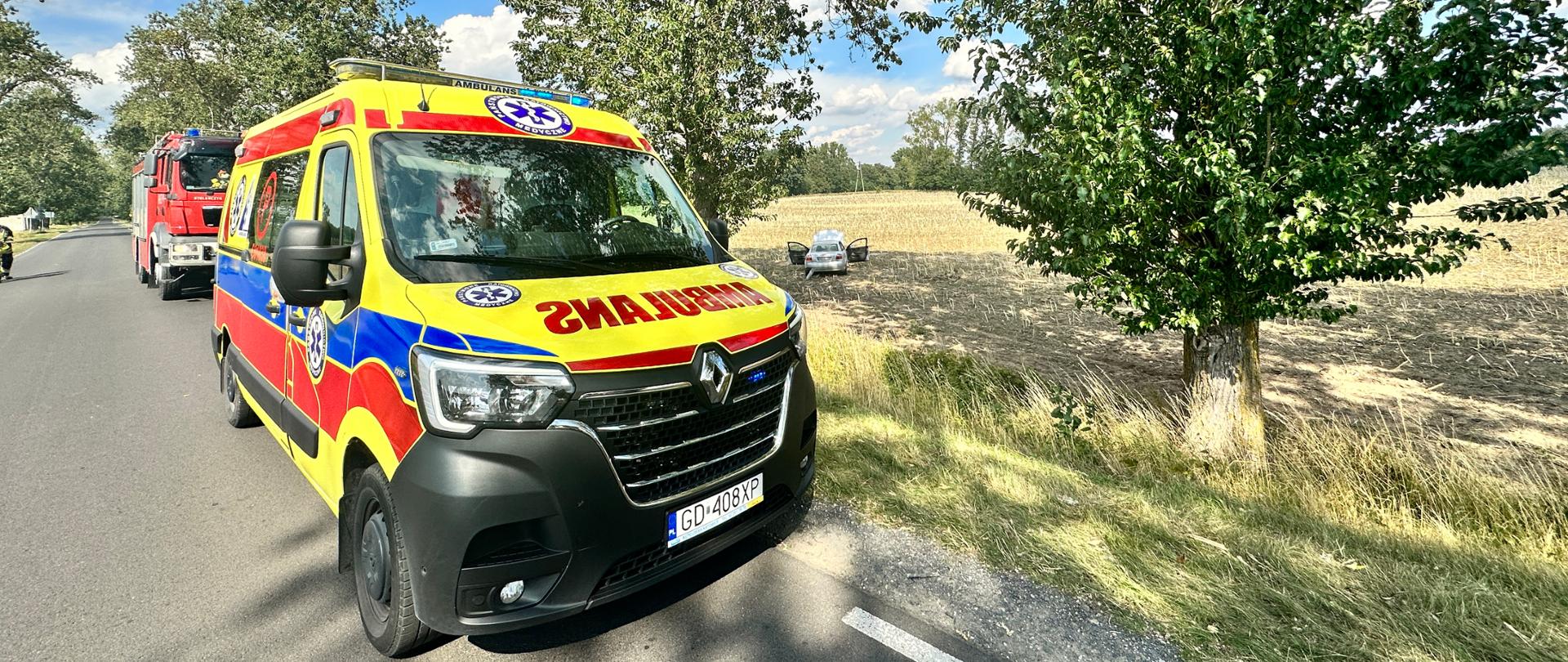Na zdjęciu znajduje się karetka, za nią stoi samochód strażacki a w polu widać samochód osobowy po uprzednim zjechaniu z drogi.