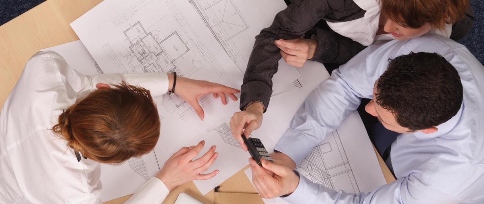 Osoby siedzące nad rysunkiem technicznym.