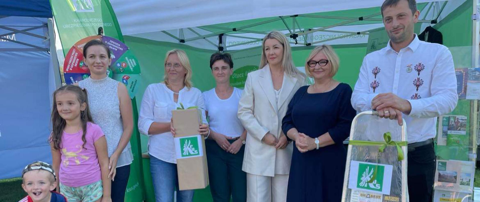 Przed stoiskiem informacyjnym pod zielonym namiotem KRUS stoi pięć kobiet, jeden mężczyzna oraz dwoje dzieci.