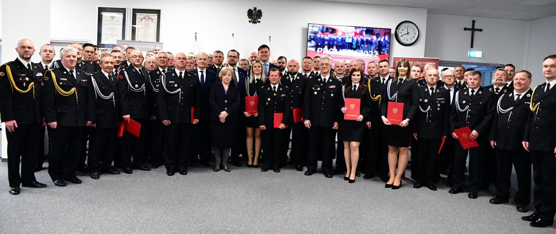 Uczestnicy uroczystości wręczenia promes i decyzji o przyznaniu świadczenia ratowniczego stoją w sali im. J. Tuliszkowskiego w KW PSP Gdańsk