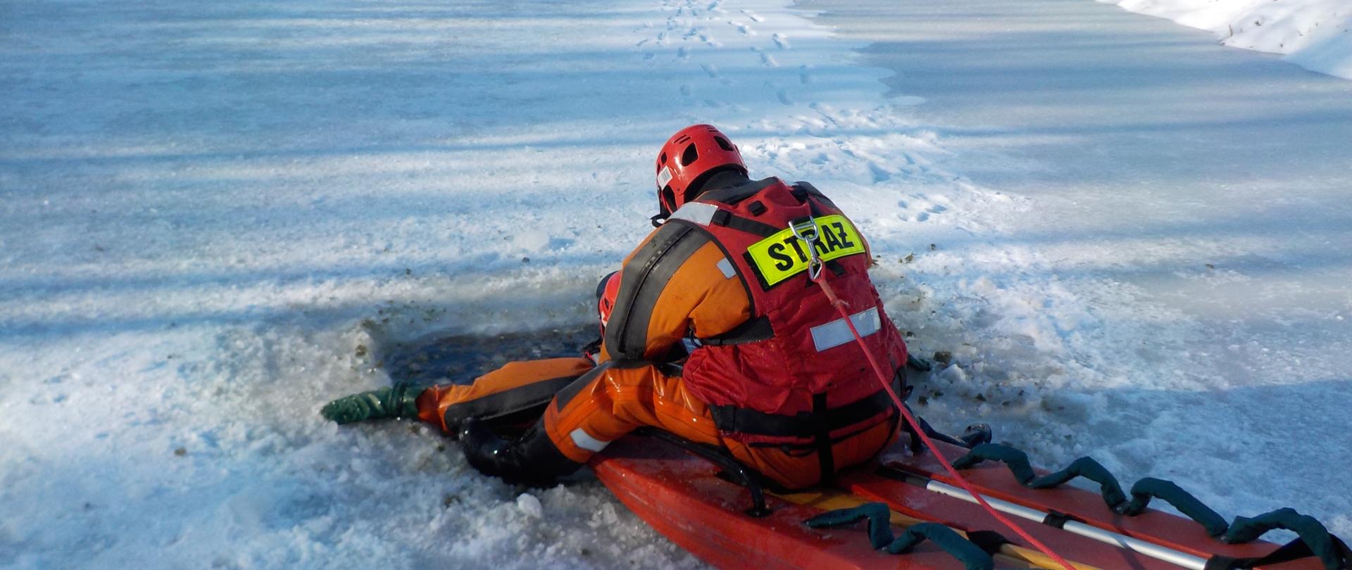 Zdjęcie przedstawia strażaka KP w Brodnicy podczas podejmowania pozoranta z przerębla z wykorzystaniem sani lodowych.