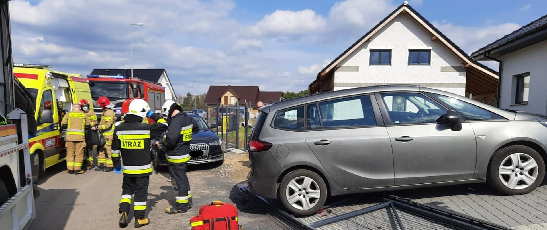 Na zdjęciu strażacy stoją przy samochodzie