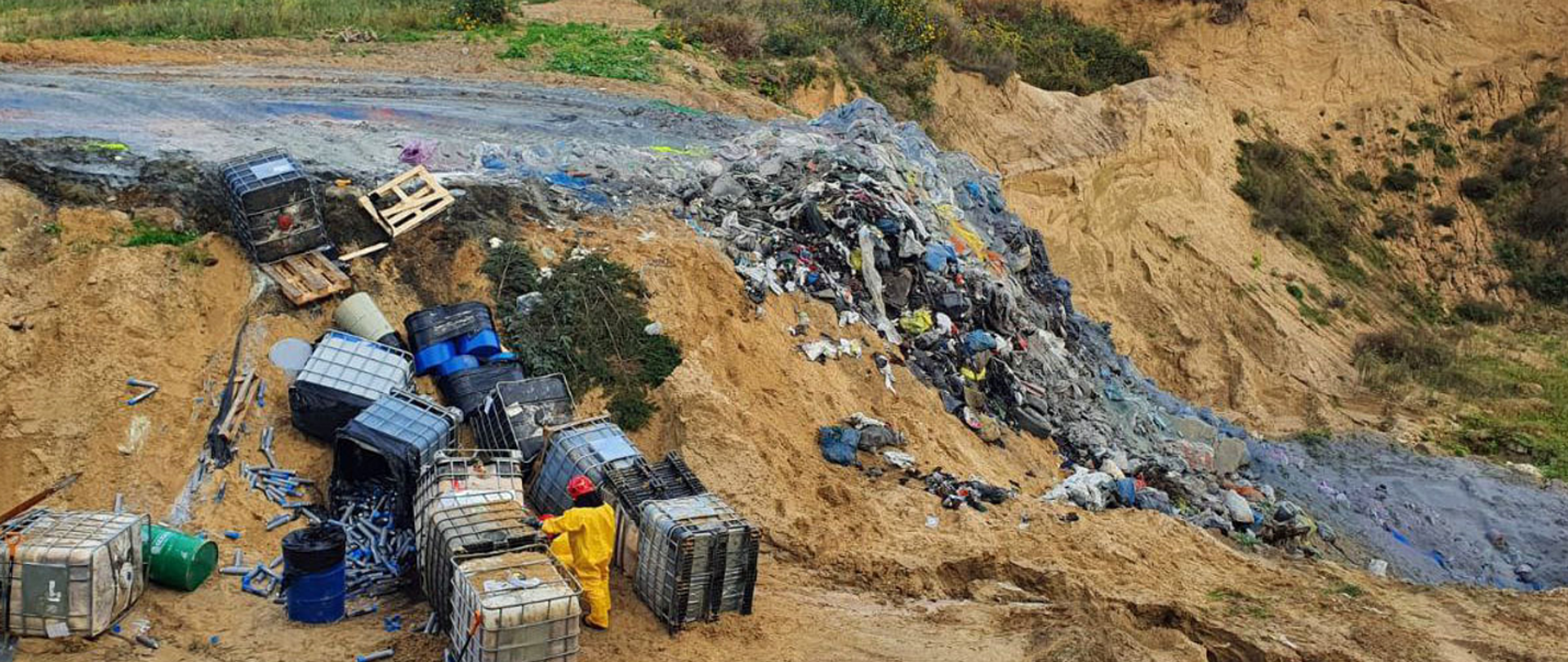 Porozrzucane w nieładzie beczki oraz śmieci komunalne na hałdzie piasku
