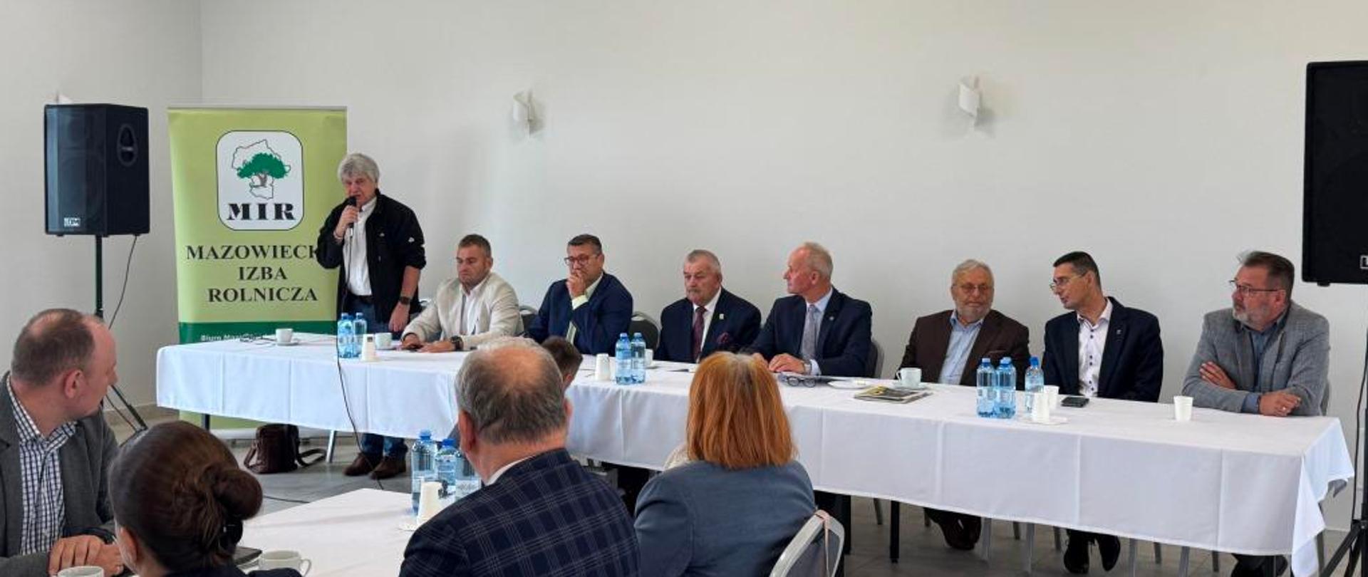 Spotkanie Mazowieckiej Izby Rolniczej w sali konferencyjnej; uczestnicy siedzą przy stołach, a jedna osoba przemawia do mikrofonu.