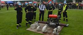 XI Powiatowe Zawody Sportowo-Pożarnicze OSP i MDP. Stadion w Miejskiej Górce. Jedna z drużyn w kategorii MDP przygotowuje się do startu do ćwiczenia bojowego. Zawodnicy stoją wokół podestu, na którym ustawiona jest motopompa oraz złożone są węże tłoczne i ssawne. Wsród nich jest prezes OSP w białej koszuli z krótkim rękawem. 