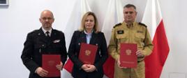 Przedstawiciele Państwowej Straży Pożarnej oraz starosta powiatu kościerskiego trzymają podpisane dokumenty.