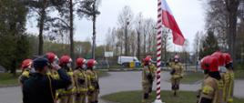 Strażacy wciągają flagę państwową na maszt.
