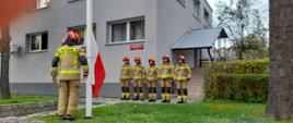 Strażacy w umundurowaniu bojowym oddający hołd przy fladze Polski