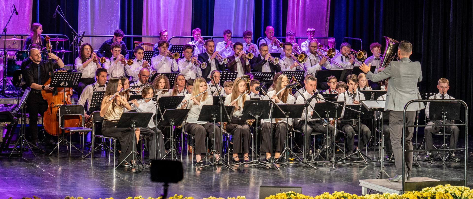 w sali widowiskowej JDK, podczas części artystycznej Jubileuszu 55–lecia PSM I st. w Jaśle, widnieje Młodzieżowa Orkiestra Dęta wraz z dyrygentem. Kolorystyka zdjęcia jest zielono-czarno-brązowo- biało-żółto- szaro-niebieska