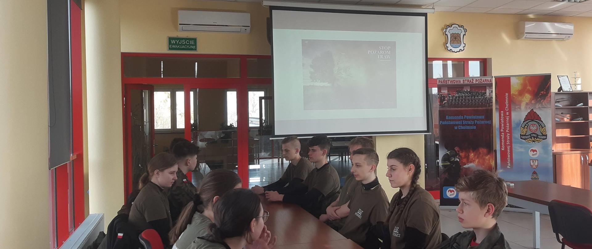 Na zdjęciu w sali sztabowej KP PSP w Chełmnie znajdują się uczniowie technikum mundurowego w Chełmnie. mł. kpt. Kasper Korczak omawia założenia kampanii społecznej "Stop pożarom traw".