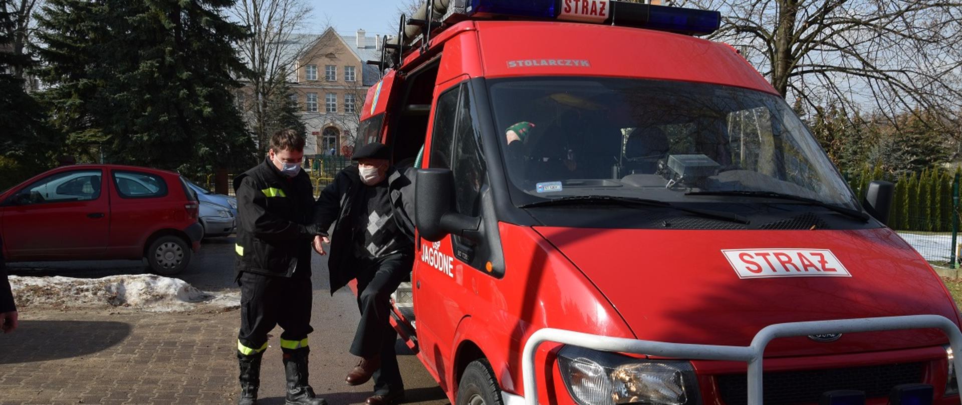 Strażak pomaga wysiąść z pojazdu pożarniczego starszemu mężczyźnie