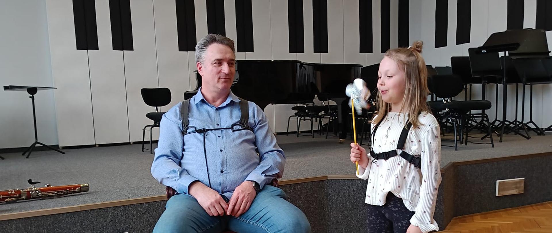 Dziewczynka dmucha w wiatraczek, obok siedzi mężczyzna.