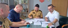 Zdjęcie przedstawia dwóch funkcjonariuszy PSP oraz samorządowców podpisujących dokumenty