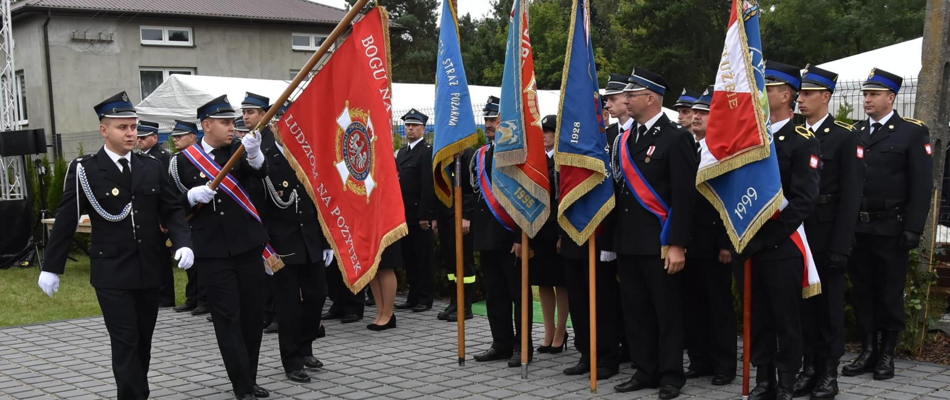Strażacy z pocztu sztandarowego z OSP w Grabcach Towarzystwo maszerują ze sztandarem wzdłuż innych pocztów sztandarowych.