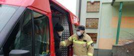 Fotografia przedstawiająca strażaka z OSP Nowy Dwór pomagającego wysiąść starszemu mężczyźnie z samochodu strażackiego bus i dotarcia do SP ZOZ w Jastrzębiu w celu szczepienia w ramach Narodowego Programu Szczepień przeciw COVID-19.