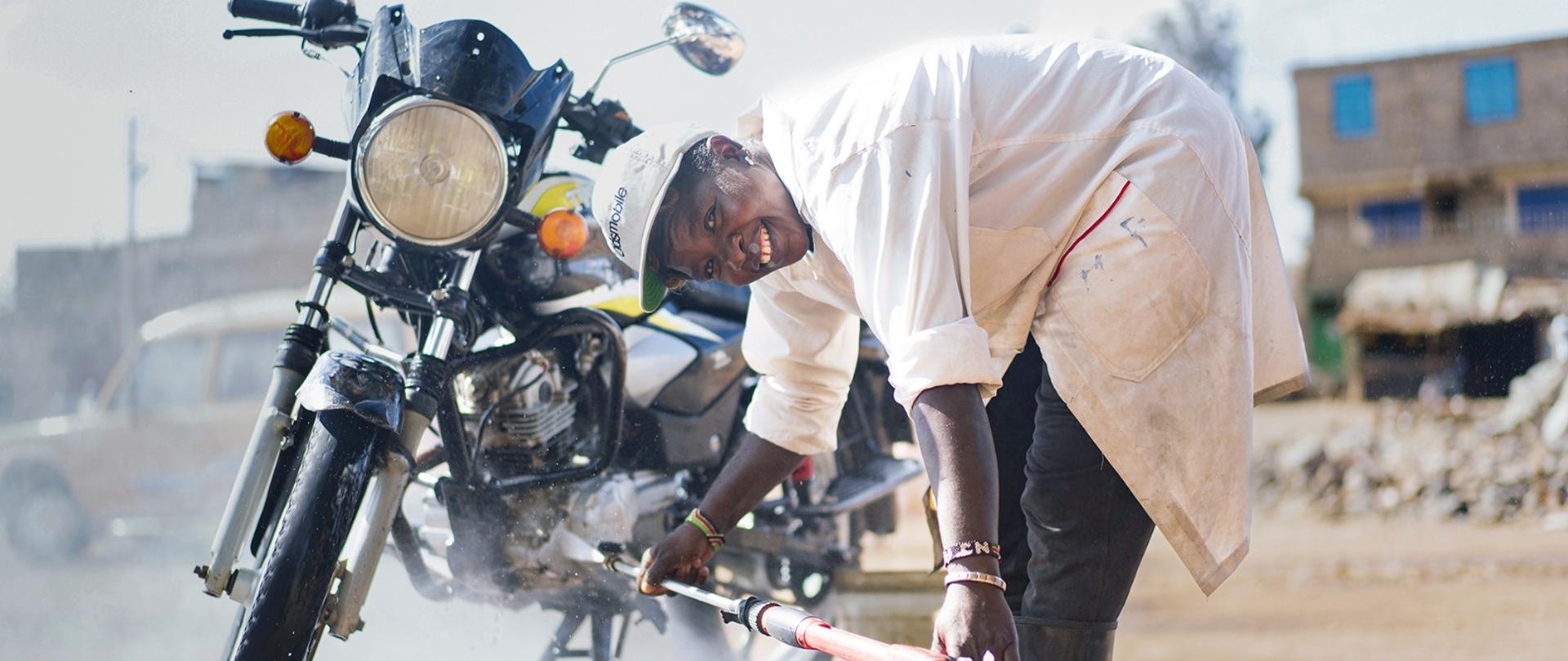 Mężczyzna myje motor woda z węża i jednocześnie uśmiecha się do kamery