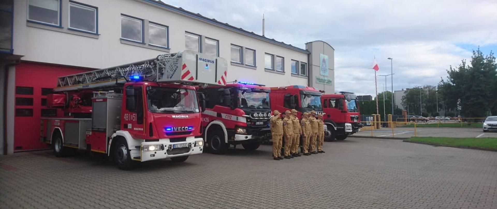 Na zdjęciu zmiana służbowa oddająca honor w rocznicę wybuchu Powstania Warszawskiego. Załoga stoi na placu przed budynkiem KP PSP w Pabianicach. Samochody pożarnicze są wyprowadzone przed garaże.