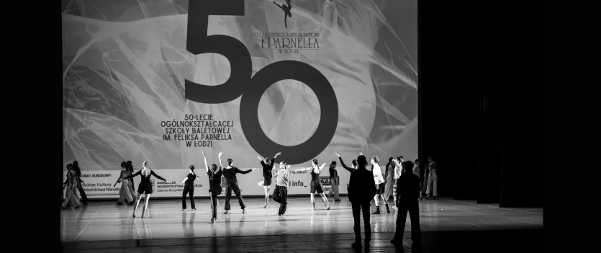 zdjęcie: n czarno białym zdjęciu widoczna próba sceniczna do gali jubileuszowej 50-lecia szkoły baletowej w Łodzi. Na scenie stoją uczniowie wraz z pedagogami tańca 