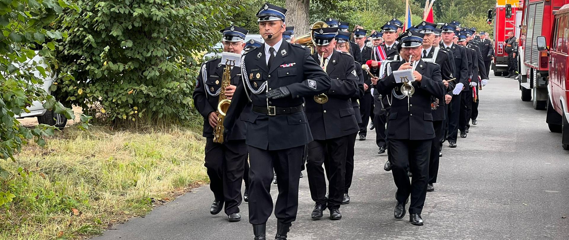 Zdjęcie przedstawia przemarsz kompanii ochotniczej straży pożarnej oraz orkiestry.