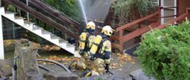 Zdjęcie przedstawia ratowników OSP podczas akcji gaszenia pożaru zwartej zabudowy drewnianych budynków w Ośrodku Wypoczynkowym