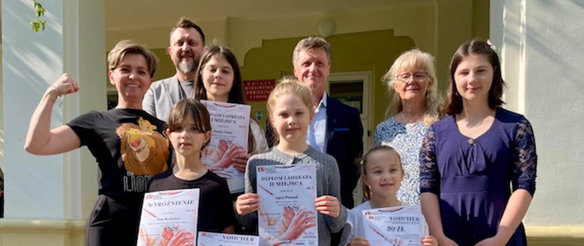 Uczennice z dyplomami i nauczyciele pozują do zdjęcia przed budynkiem szkoły po IX Podkarpackim Festiwalu Młodych Flecistów.
