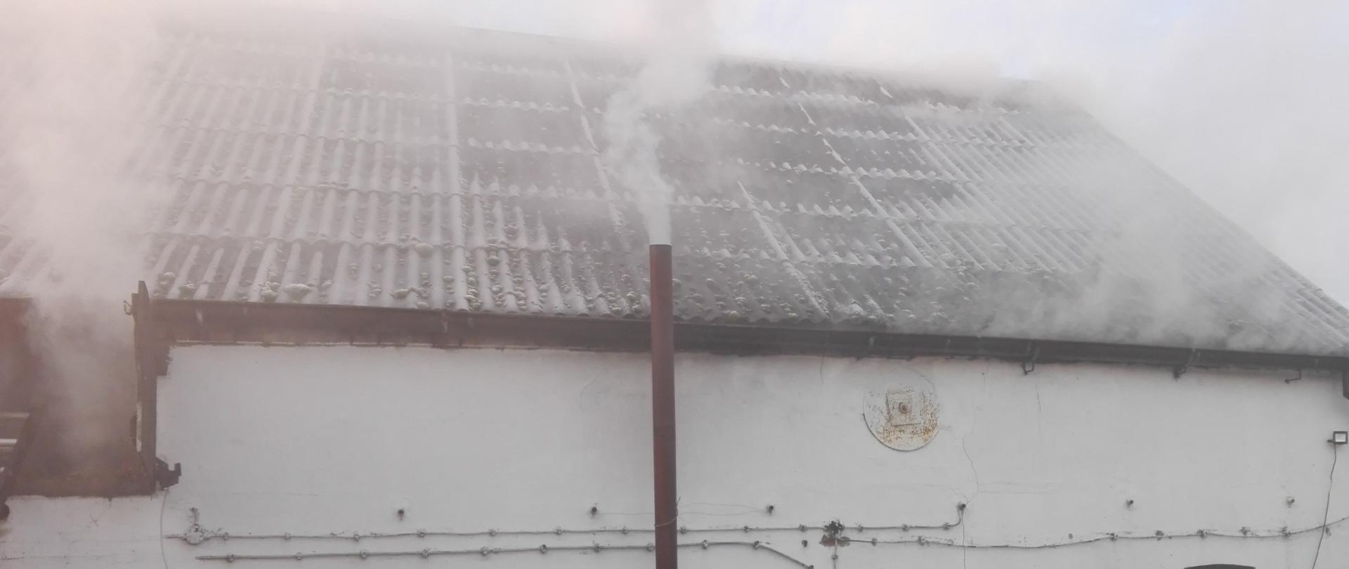Zdjęcie przedstawia zadymiony dach budynku gospodarczego