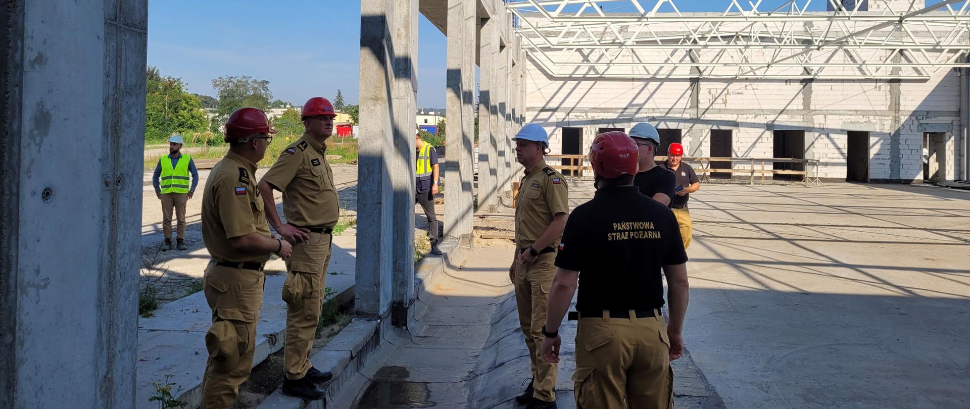 Strażacy w piaskowych mundurach służbowych na placu budowy budynku.