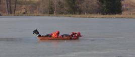 Zdjęcie przedstawia zamarznięty akwen wodny. Na saniach lodowych dwóch strażaków poruszających się po lodzie.