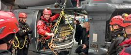 Grupa ratowników wysokościowych podczas ćwiczeń w hangarze z wykorzystaniem noszy i wyciągarki śmigłowca Black Hawk. 