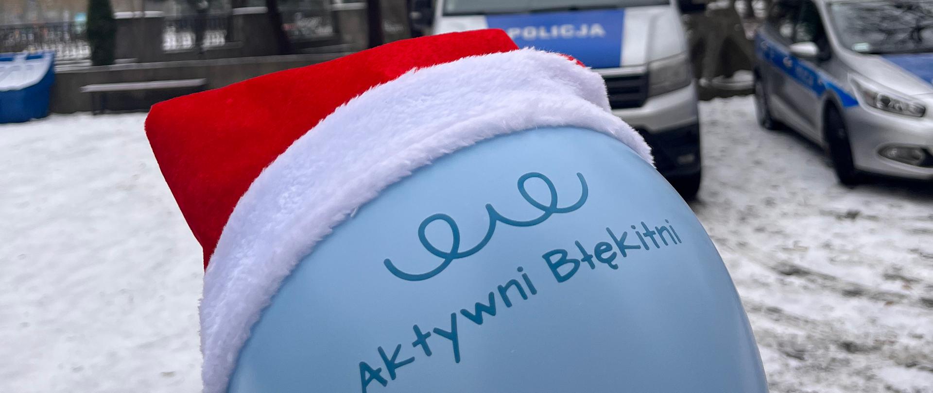 niebieski balon w czapce mikołaja na tle pejzarzu zimowego i wozu policyjnego