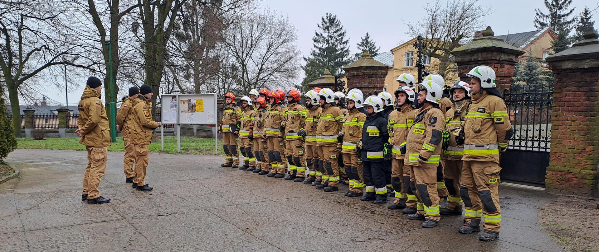 Zdjęcie przedstawia strażaków PSP oraz OSP ubranych w ubrania specjalne koloru piaskowego oraz w hełmy koloru czerwonego oraz białego, podczas ćwiczeń obiektowych w kościele Parafii Rzymskokatolickiej Wniebowzięcia NMP