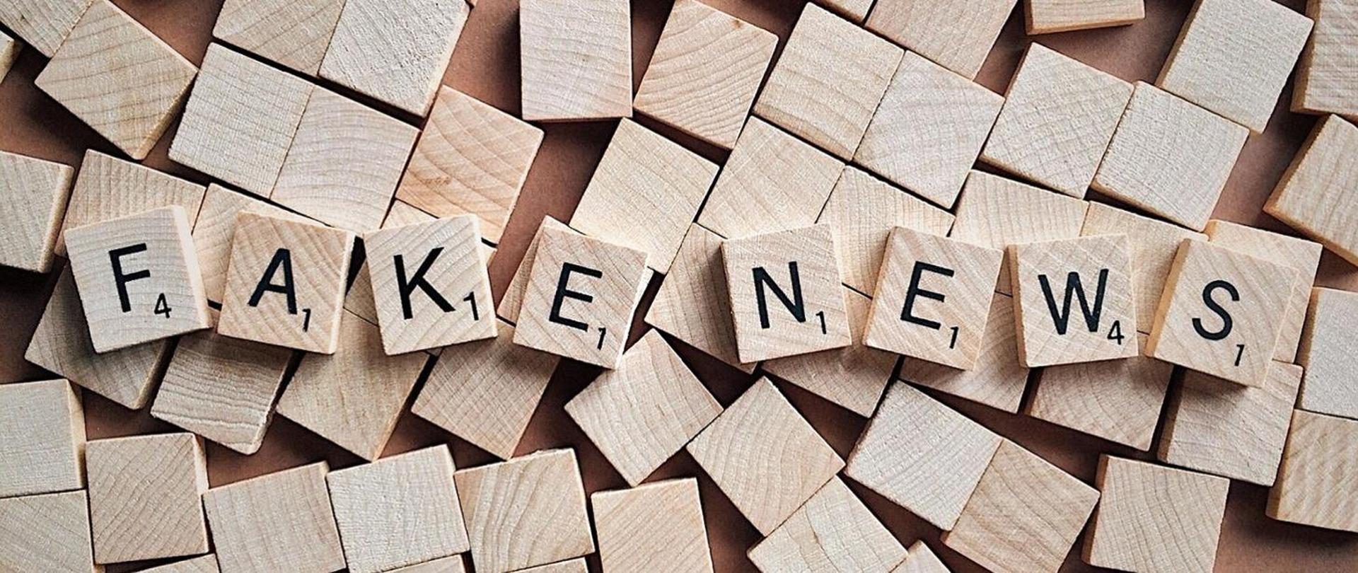 rozsypane drewniane sześciany , po środku zdjęcia ułożone w jednej linii sześciany z literami układającymi się w napis fake news 
