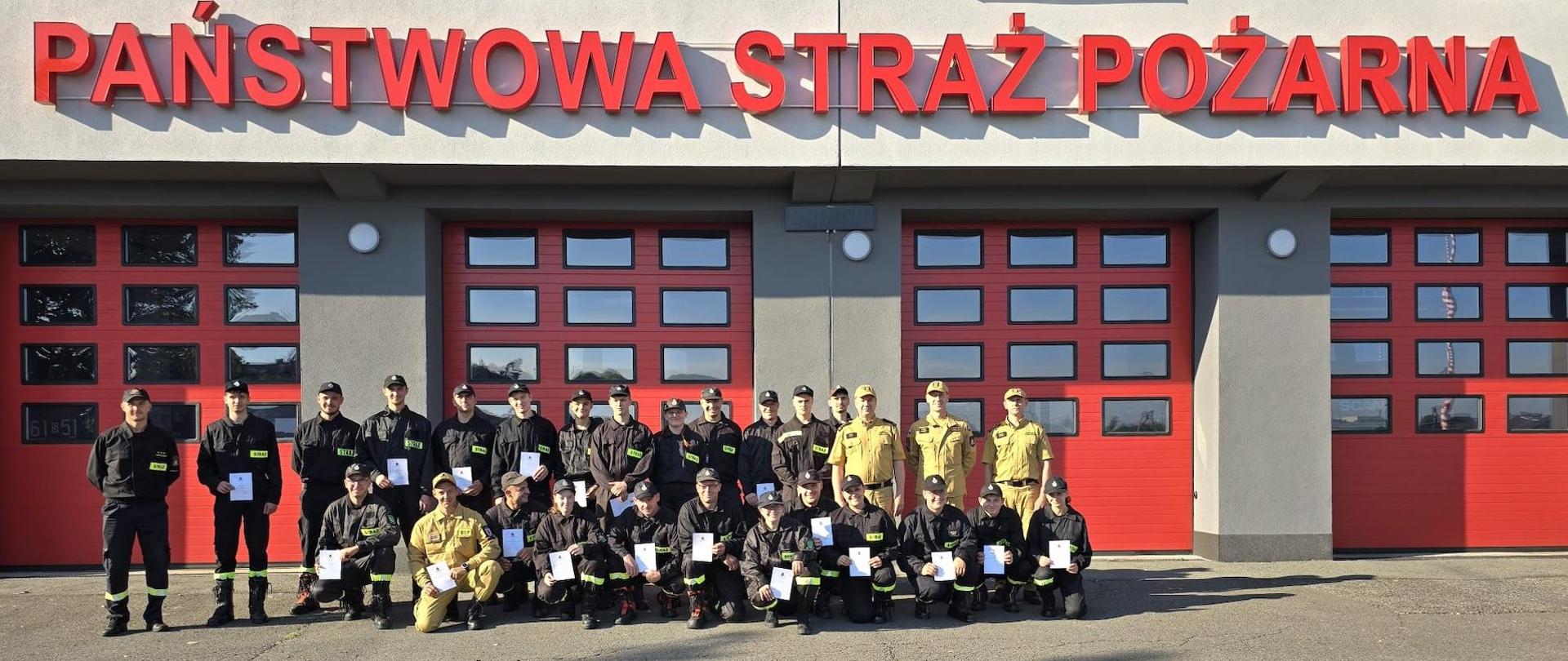 Absolwenci kursu na zdjęciu grupowym na tle budynku komendy