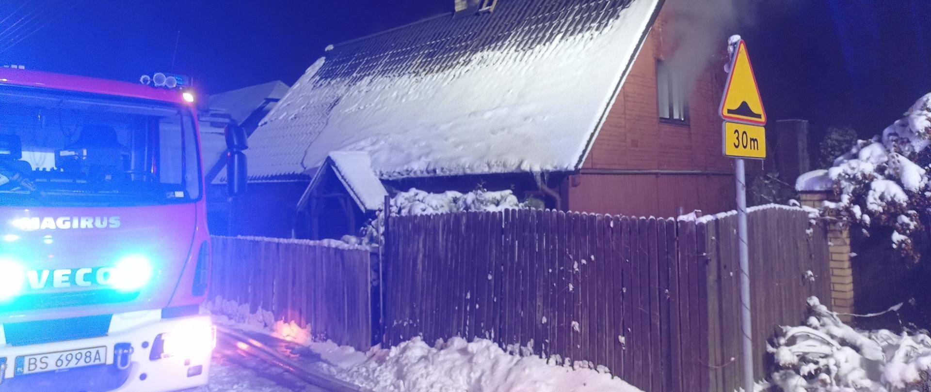 Z domu wydobywa się dym, obok stoi samochód gaśniczy 