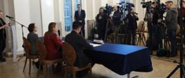 Na zdjęciu minister Katarzyna Pełczyńska-Nałęcz siedzi za stołem konferencyjnym i odpowiada na pytania dziennikarzy w towarzystwie innych uczestników spotkania