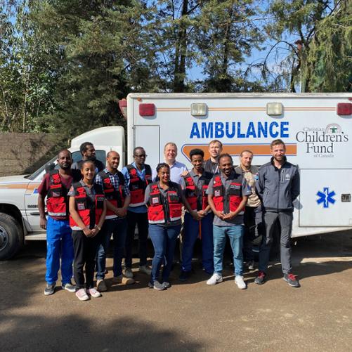 Ratownicy medyczni pozujący do zdjęcia na tle ambulansu.