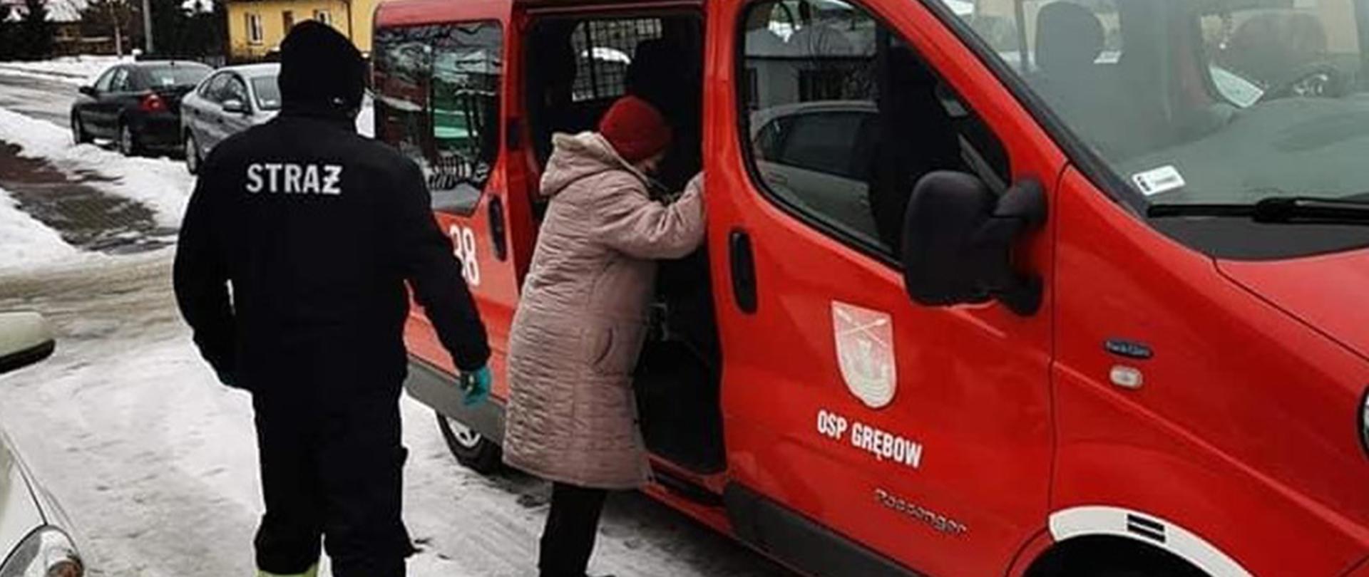 Na zdjęciu: strażacy pomagają starszej kobiecie w wejściu do samochodu 