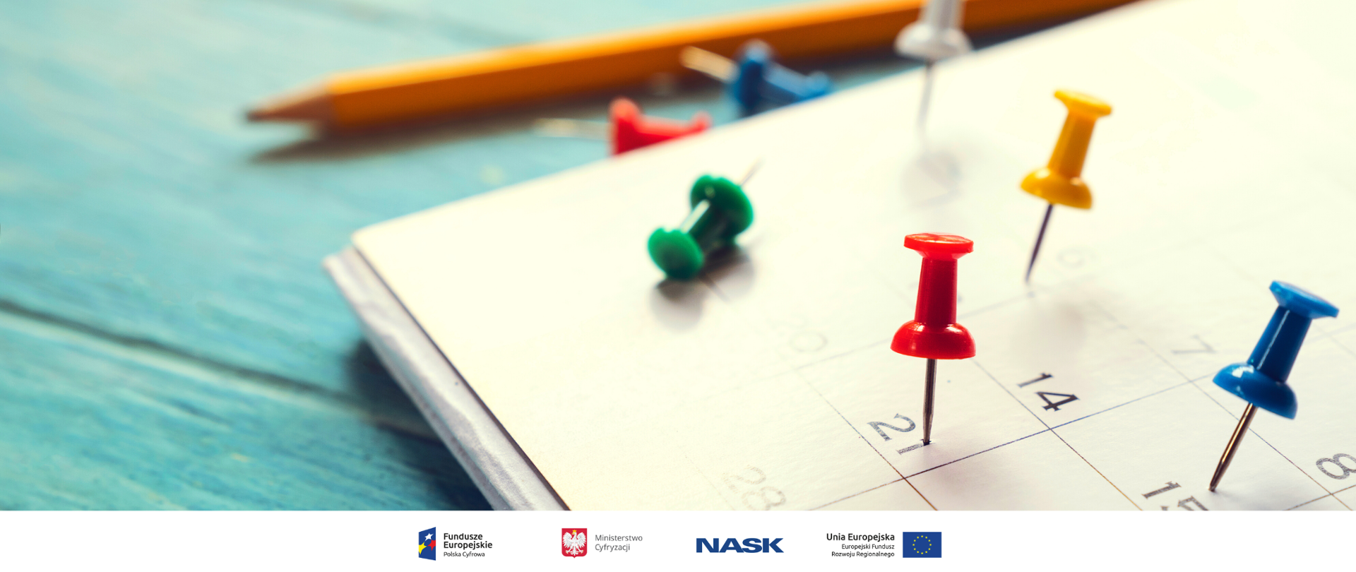 Zdjęcie leżącego na stole kalendarza. W różne daty powbijane są różnokolorowe pinezki. 