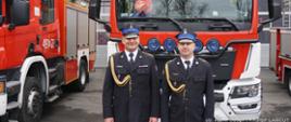 Na zdjęciu widocznych jest dwóch funkcjonariuszy PSP w Łańcucie, którzy przechodzą na zaopatrzenie emerytalne na tle Komendy oraz samochodów ratowniczo-gaśniczych.