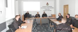 Zdjęcie dotyczy narady szkoleniowej grup specjalistycznych. W sali narad przy stołach siedzi 8 funkcjonariuszy w mundurach oraz jeden funkcjonariusz, który stoi przy komputerze i przedstawia prezentację. Na zdjęciu Zastępca Świętokrzyskiego Komendanta Wojewódzkiego Państwowej Straży Pożarnej starszy brygadier Jarosław Piotrowski, koordynatorzy poszczególnych grup specjalistycznych województwa świętokrzyskiego oraz kadra Ośrodka Szkolenia Komendy Wojewódzkiej Państwowej Straży Pożarnej w Kielcach. W tle z projektora wyświetlane tabele szkoleniowa poszczególnych grup specjalistycznych