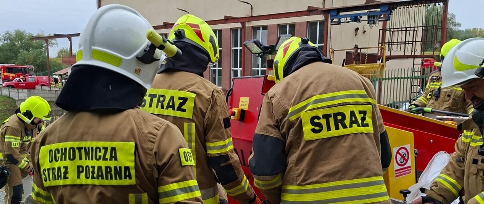 Grupa strażaków z PSP i OSP napełnia worki piachem. 