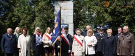 15 osób zgromadzonych pod pomnikiem. Pośrodku poczet sztandarowy. 