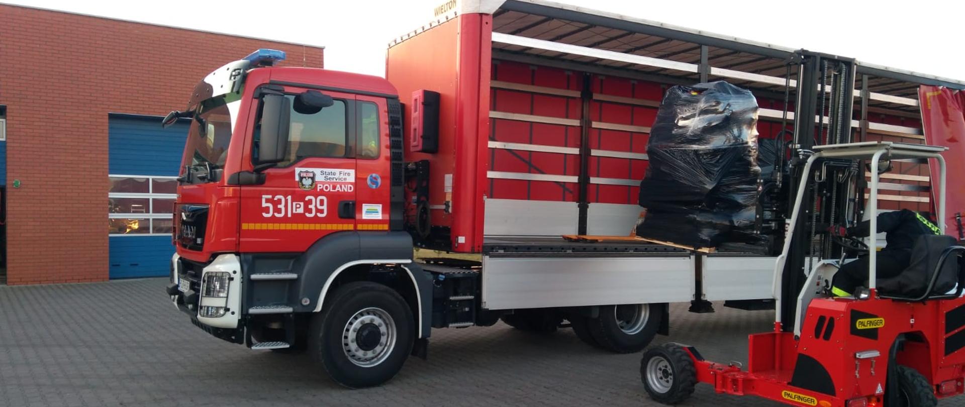 Proces ładowania sprzętu ratowniczo-gaśniczego wózkiem widłowym na naczepę samochodu ciężarowego - strażackiego. 