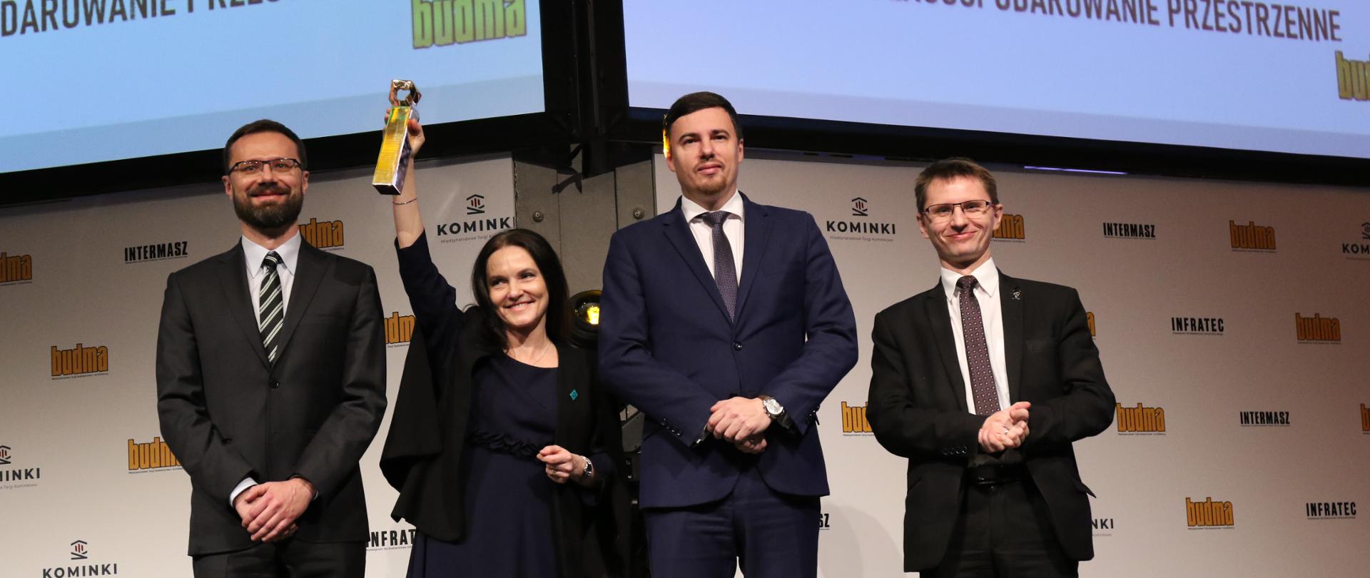 Targi Budma - wiceminister Robert Nowicki stoi na scenie z laureatami nagrody.