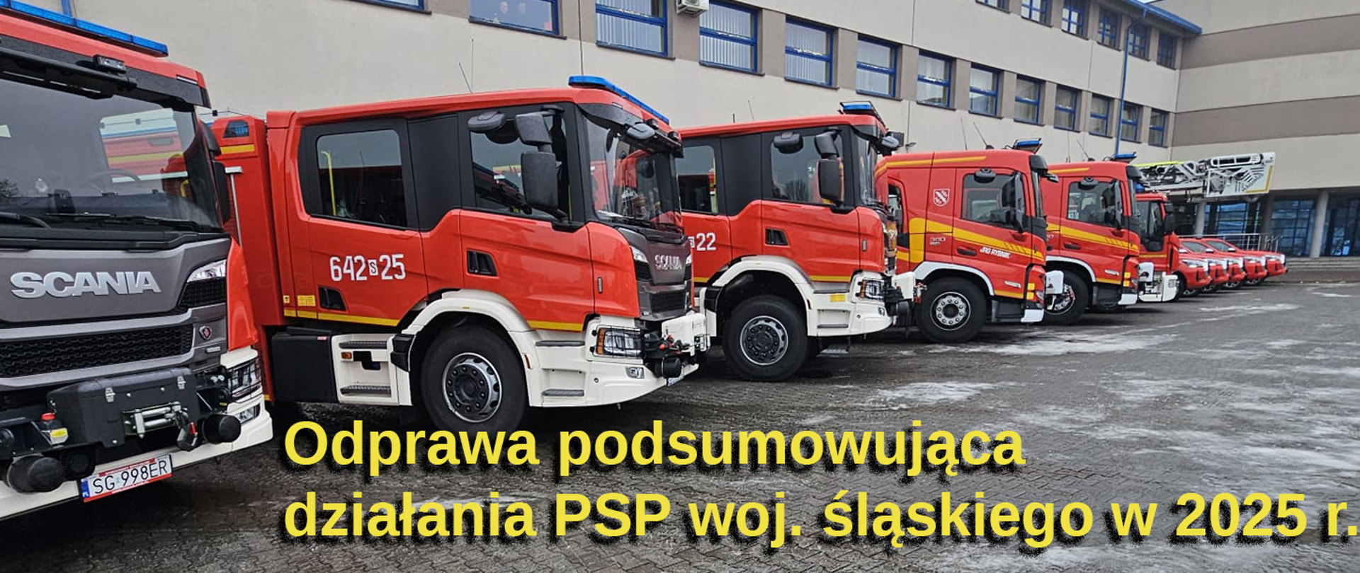 Rząd czerwonych samochodów ratowniczo-gaśniczych Państwowej Straży Pożarnej zaparkowanych przed budynkiem komendy.