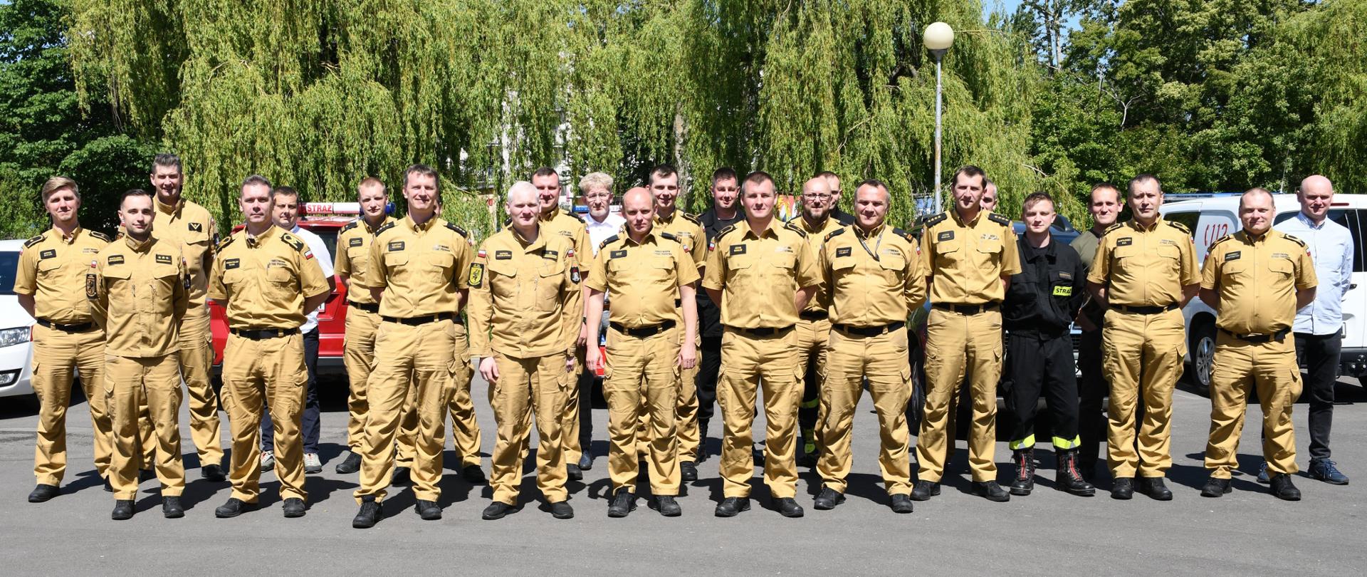 Strażacy oraz osoby postronne stoją obok siebie w dwóch rzędach.